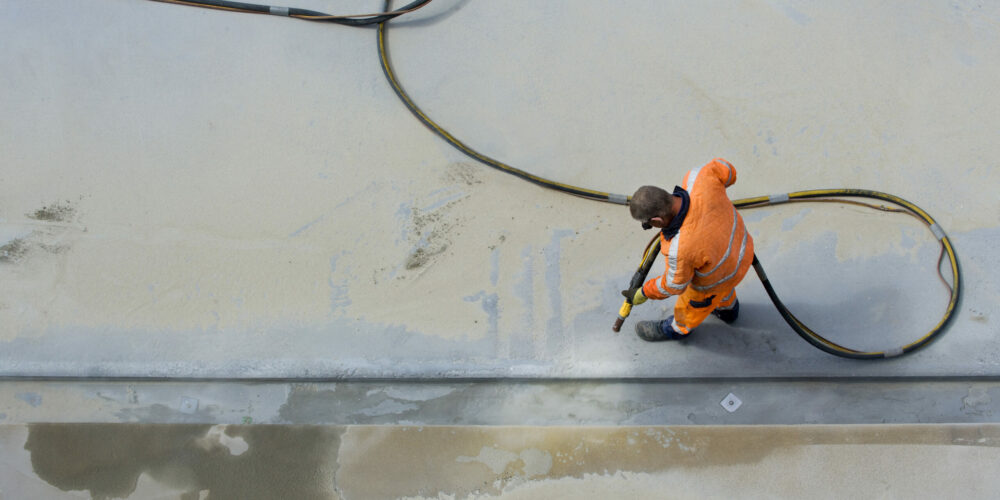 Sandblasting Man in orange workclothes sandblasting concrete surface with airpressure hose. Photographed from above.